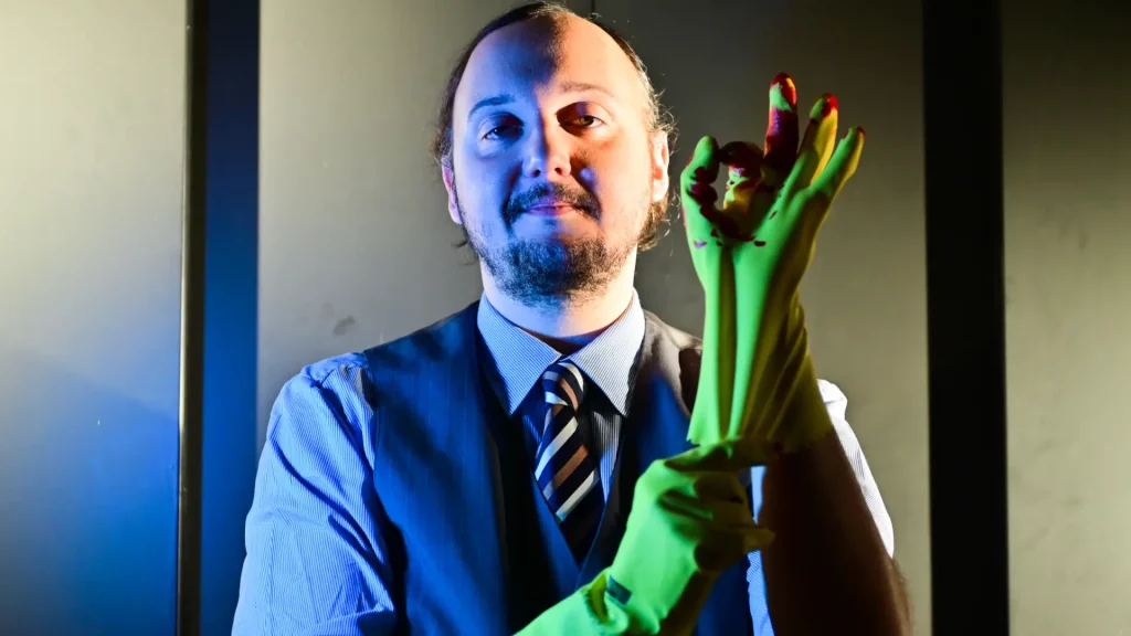 Ein Darsteller zieht sich einen blutverschmierten Reinigungshandschuh an